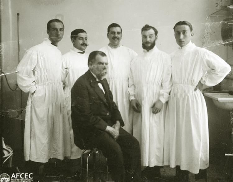 El professor de Cirurgia, Àlvar Esquerdo i Esquerdo, assegut al centre de la imatge, envoltat del seu equip d’ajudants entre els quals es troba el jove Òscar Torras i Buxeda, a la dreta de la imatge. Servei de Cirurgia de l’antic Hospital de la Santa Creu. Barcelona, c. 1912